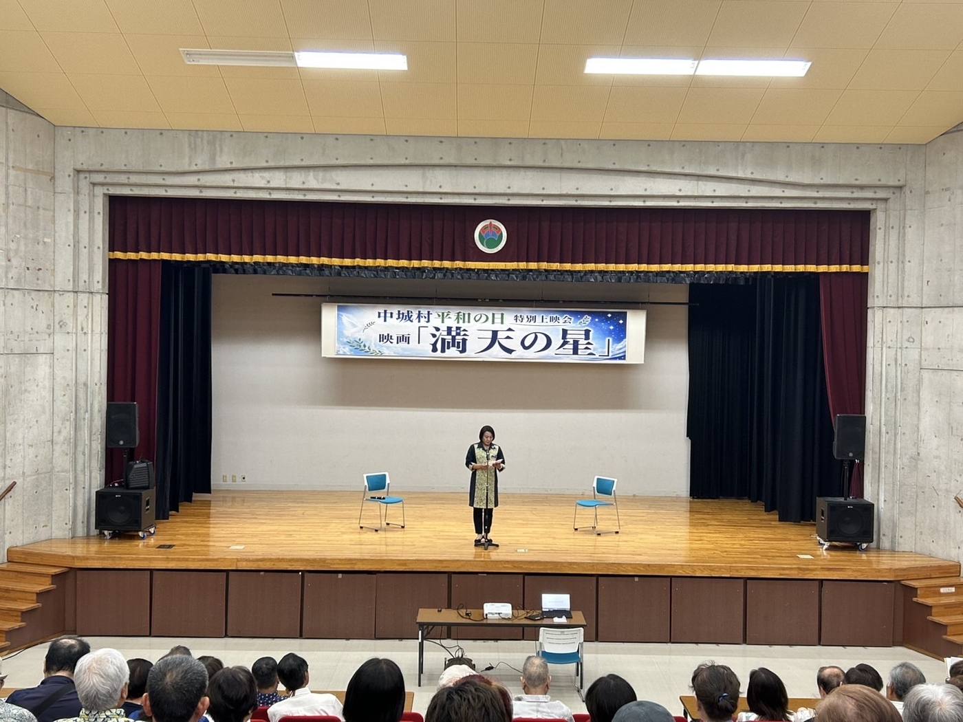 客席から見た会場のステージ。中央に登壇者が立ち、背後に上映会の横断幕が掲げられている